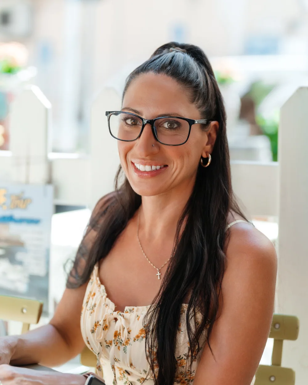 Carla smiling over her laptop at an outdoor cafe table in Sicily