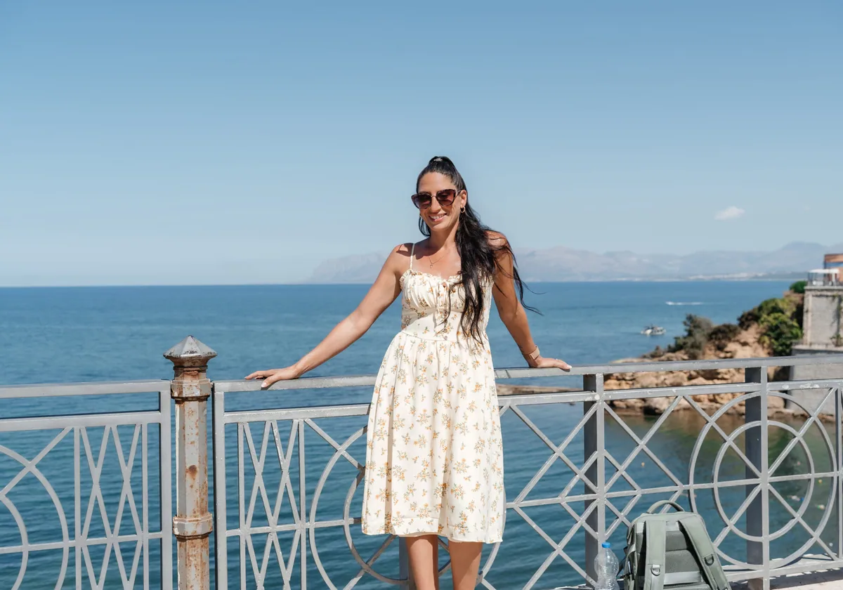 Carla leaning on a seafront railing with the gulf and headlands behind her