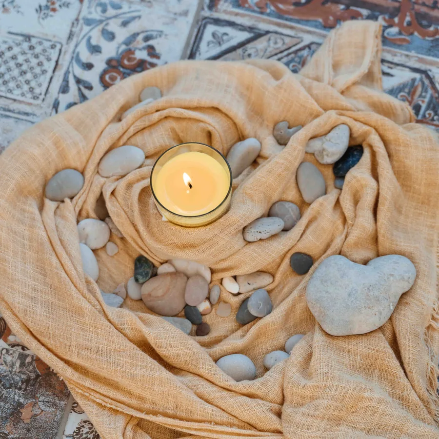 A candle and smooth stones arranged on cloth over patterned Sicilian tile