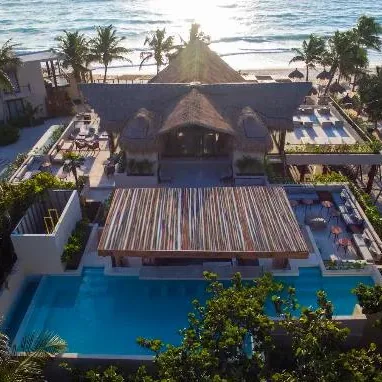 A beach club pool and palapa roof on the Tulum shoreline from above