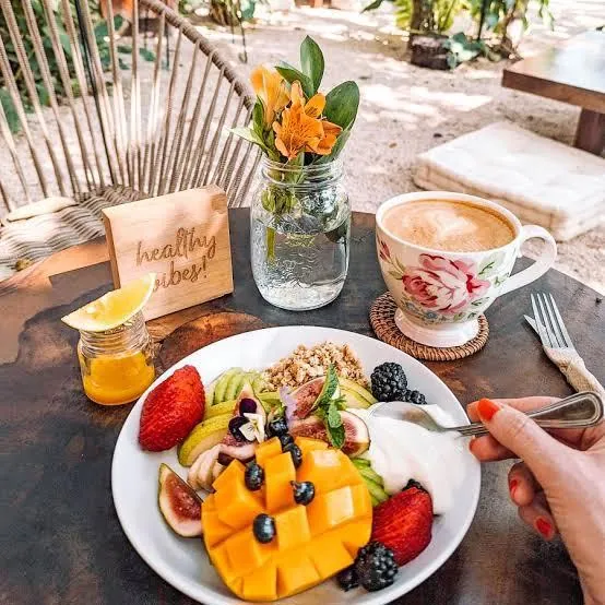 A breakfast of mango, berries and a latte at a table in the sun