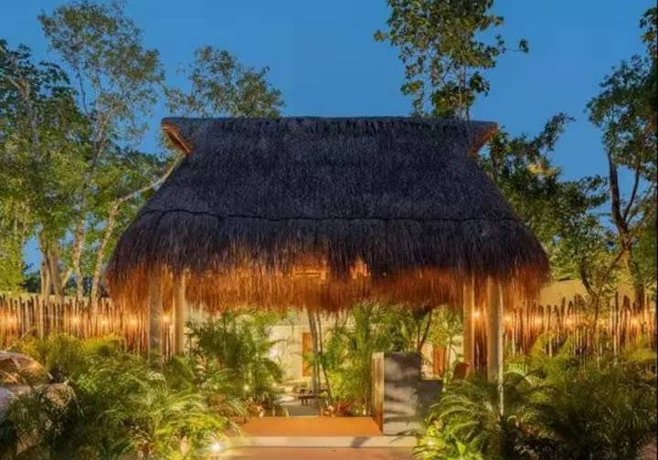 A thatched palapa glowing at dusk among the palms