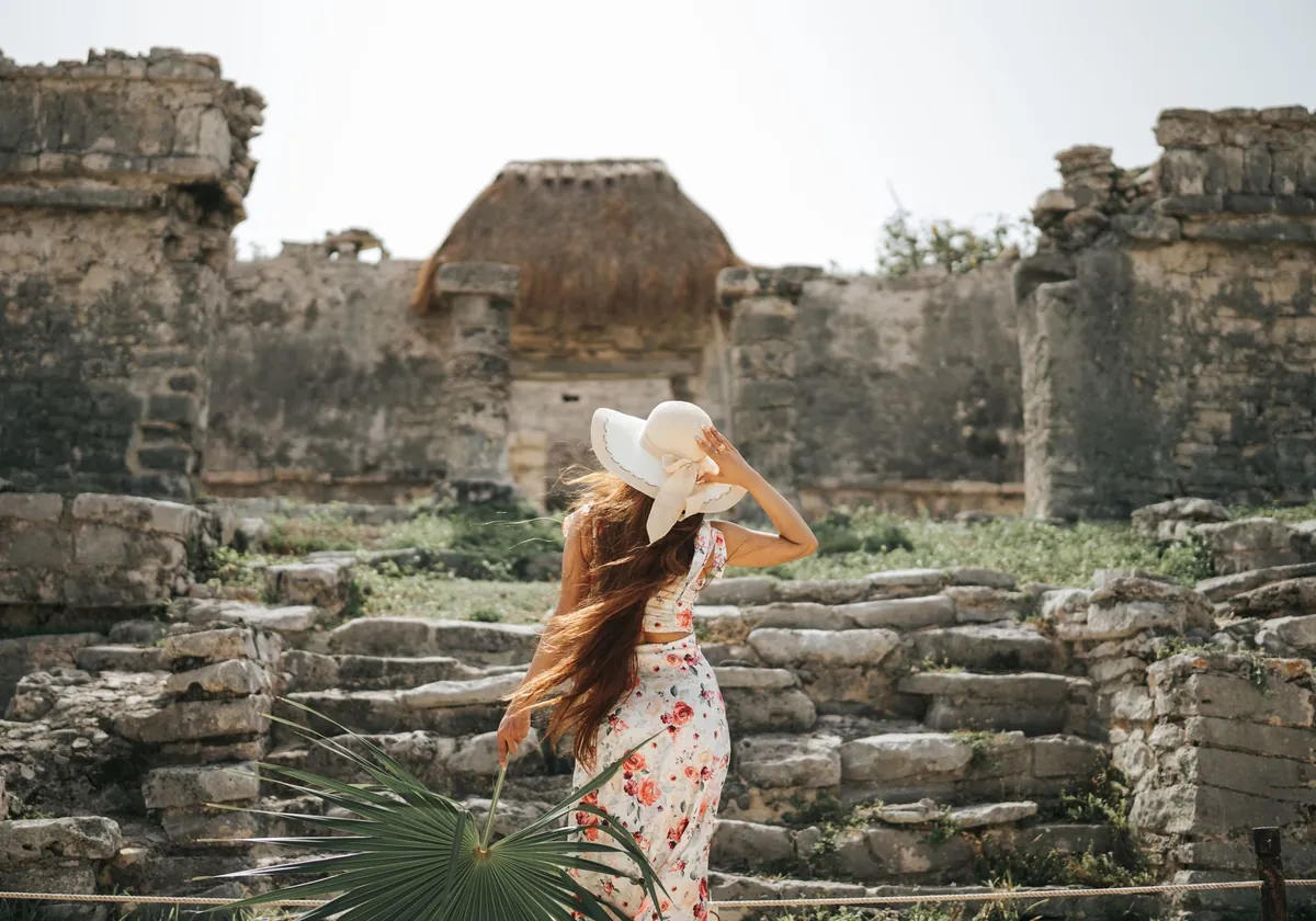 A woman in a wide sun hat taking in the Mayan ruins at Tulum